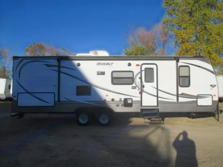 This white and gray travel trailer, ideal for RV rental, is parked outside on a sunny day. Features a large side slide-out.. Keystone Hideout 2014