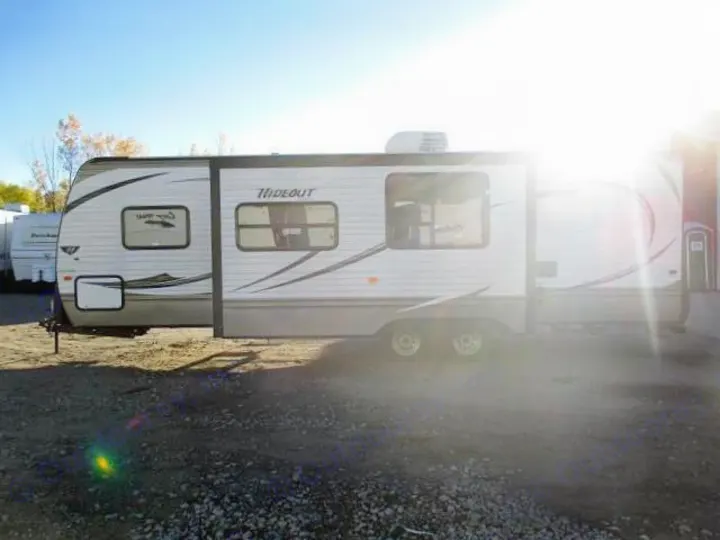 A white Hideout travel trailer, an RV rental, is pictured outdoors with its slide-out extended.. Keystone Hideout 2014