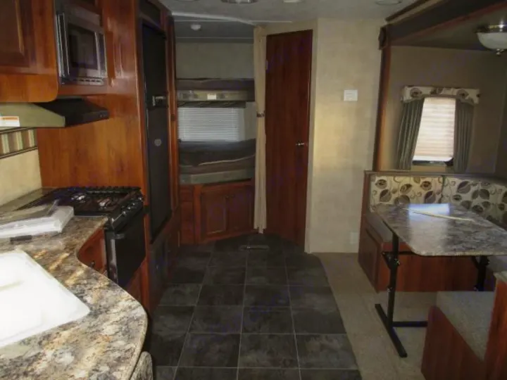 Inside an RV rental: View of the kitchen with appliances, a dinette table, and bunk beds in the rear.. Keystone Hideout 2014