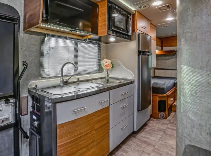 Step into this cozy rv rental featuring a compact kitchen with a sink, microwave, and fridge, extending to a comfortable bedroom area.. Winnebago View 2016