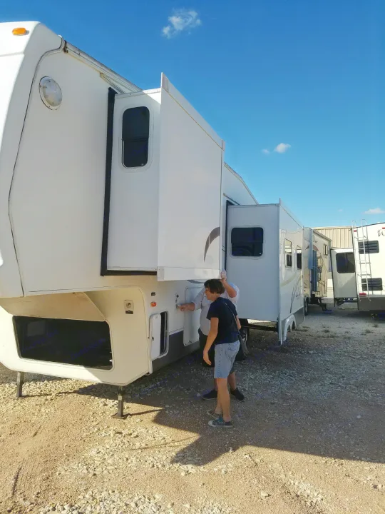 RV rental inspection: Two people check a large white travel trailer with its slide-out extended on a sunny gravel lot.. Forest River Cedar Creek Silverback Edition 2005