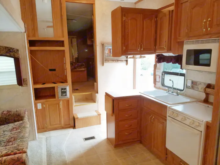 Inside an RV rental: a well-equipped kitchen with wood cabinets, sink, microwave, and stove, beside a cozy living space.. Forest River Cedar Creek Silverback Edition 2005