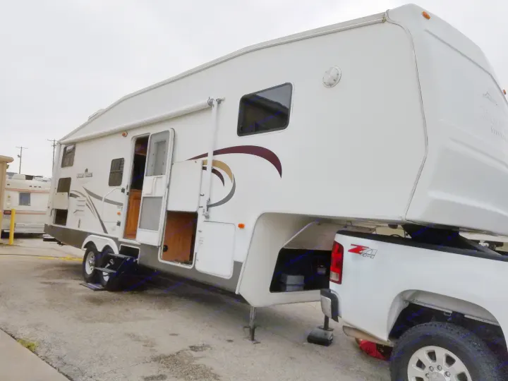 White fifth-wheel RV rental, hitched to a pickup truck, with doors and storage compartments open, ready for travel.. Forest River Cedar Creek Silverback Edition 2005
