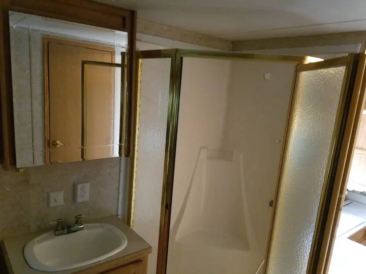 RV rental bathroom features a compact sink, mirror, and a shower with textured glass doors.. Forest River Cedar Creek Silverback Edition 2005