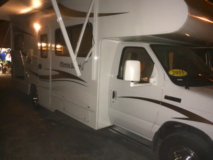 A white Winnebago Minnie Winnie RV rental, model year 2015, with its awning extended, parked indoors.. Winnebago Minnie Winnie 2015