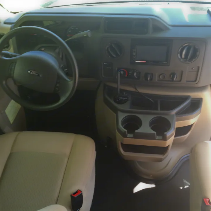 RV rental front cabin showing Ford steering wheel, dashboard, and central console with cup holders.. Winnebago Minnie Winnie 2015