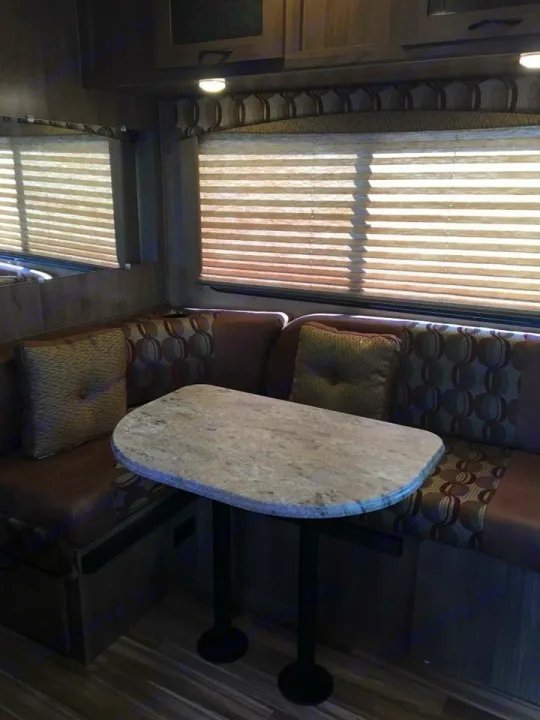Cozy rv rental dinette featuring a booth with patterned cushions, a light table, and windows with blinds.. Coachmen Freelander 2016