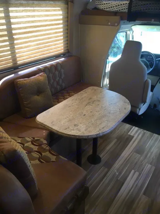 Spacious RV rental interior with a bright dinette, upholstered booth seating, stone-look table, and wood-grain flooring.. Coachmen Freelander 2016
