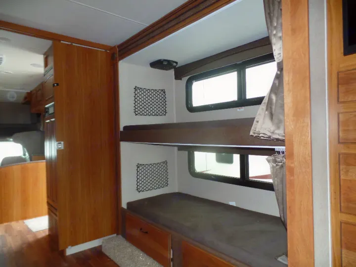 Inside an **RV rental**, showing a bunk bed area with windows and nets, looking towards the kitchen/living space.. Jayco Greyhawk 2016