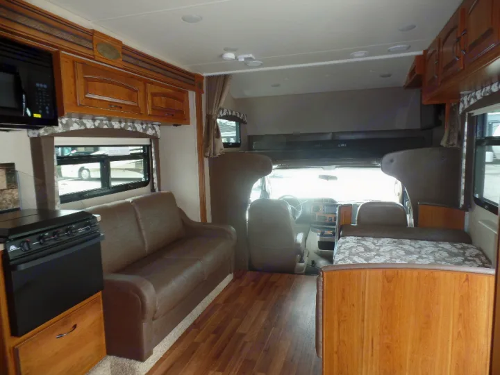 Interior of an RV rental: kitchen with microwave (left), brown sofa (center), and driver's cockpit (front).. Jayco Greyhawk 2016