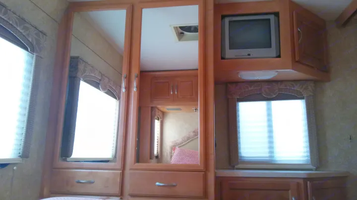 Inside an RV rental: view of the bedroom area with wood cabinetry, a TV, and mirrors, offering a cozy travel experience.. Chevrolet Dutchmen 2007