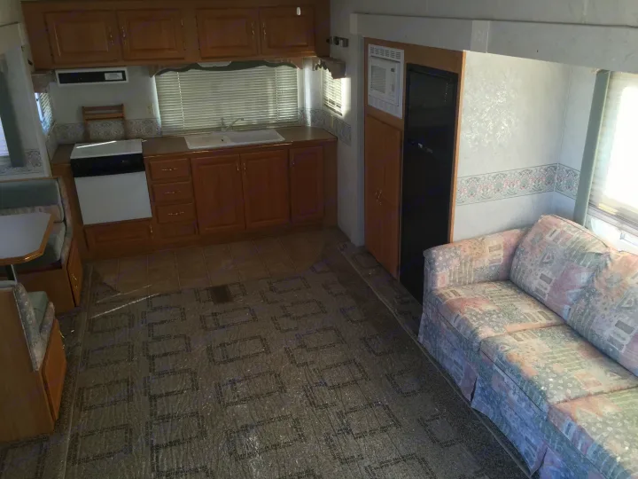 RV rental's spacious interior: kitchen with stove/sink, dining booth, and a patterned sofa. Floor covered in protective film.. Holiday Rambler Alumascape 2002