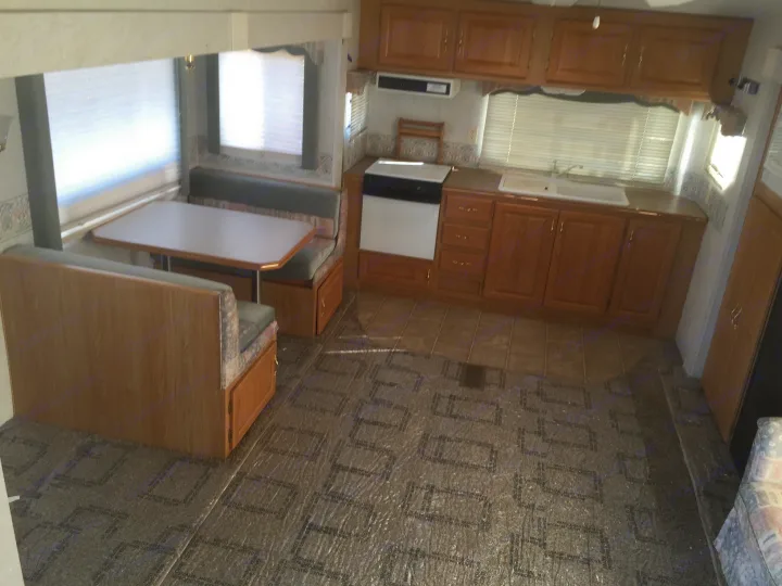 Inside an RV rental, showing a cozy dinette, kitchen with wood cabinets, and patterned floor under protective film.. Holiday Rambler Alumascape 2002