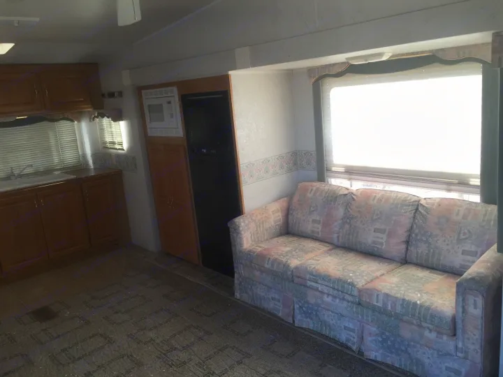 RV rental interior featuring a kitchen with wood cabinets, sink, and appliances, leading to a living area with a patterned sofa and large window.. Holiday Rambler Alumascape 2002