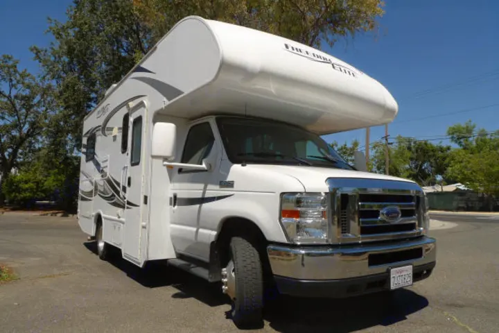 A bright white Class C motorhome, ready for an rv rental, parked on asphalt with trees and blue sky.. Forest River Freedom 2013