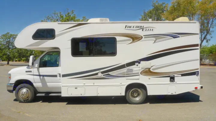 Side profile of a white Class C RV rental (Freedom Elite model) parked on asphalt. Features dark windows and decorative decals.. Forest River Freedom 2013