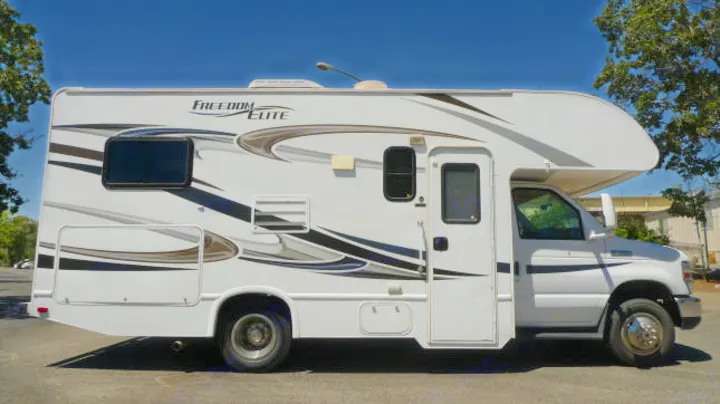 Side view of a white Class C motorhome with "Freedom Elite" decals, ideal for an rv rental adventure.. Forest River Freedom 2013