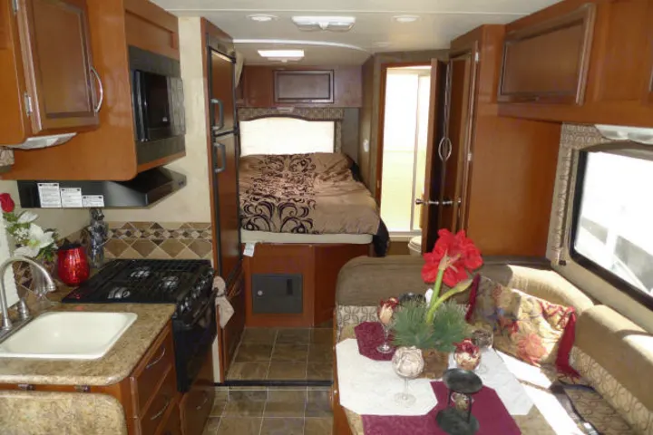 Explore this cozy RV rental interior featuring a compact kitchen, comfortable bed, and dining/lounge area.. Forest River Freedom 2013