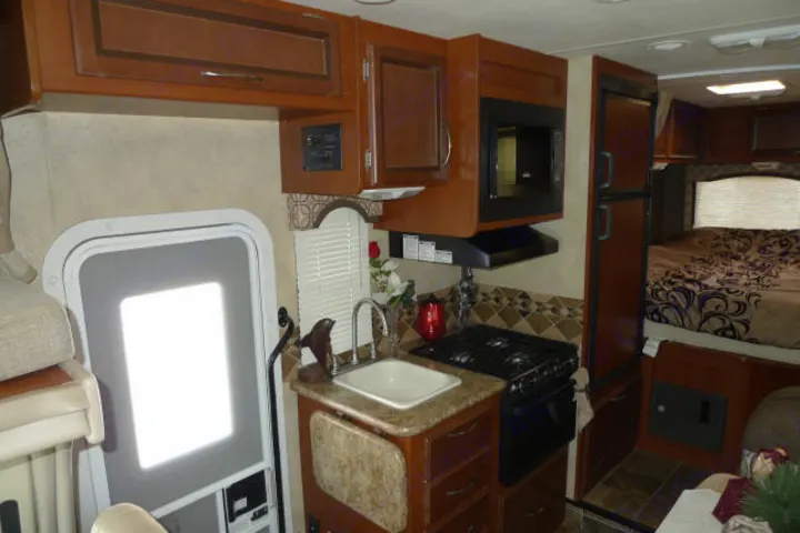 Spacious RV rental interior featuring a full kitchen with microwave, stove, sink, and a comfortable bed in the back.. Forest River Freedom 2013