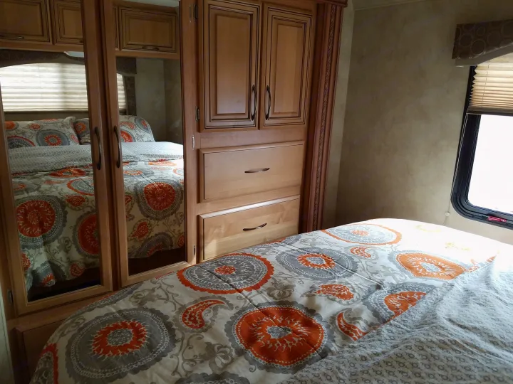 RV rental bedroom interior: Bed with orange/gray comforter, wood storage unit with mirrors, and window.. Thor Motor Coach Chateau 2011