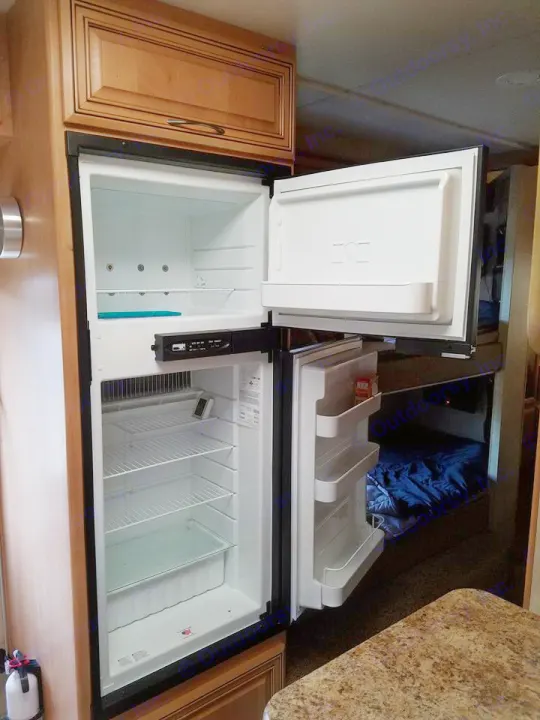 Open RV refrigerator and freezer interior, featuring shelves and door storage, beside a bunk bed area. An RV rental feature.. Thor Motor Coach Chateau 2011