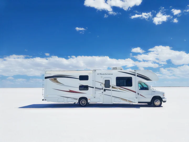 An rv rental, a white motorhome with decals, stands alone on a vast, bright white salt flat under a clear blue, cloudy sky.. Thor Motor Coach Chateau 2011