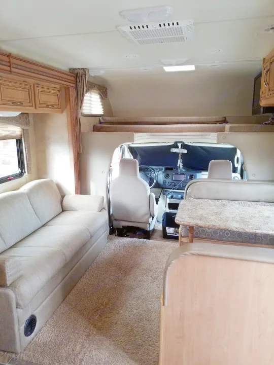 RV rental interior showing a sofa, dinette table, and cockpit view. An overhead bunk is visible, offering a spacious living area.. Thor Motor Coach Chateau 2011