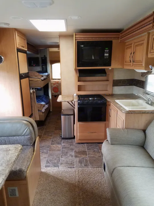 Spacious RV rental interior features a full kitchen, bunk beds, dinette, and sofa, perfect for comfortable family travel.. Thor Motor Coach Chateau 2011