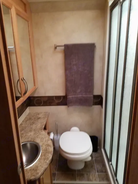 RV rental bathroom with sink, toilet, shower, and mirrored cabinet. Compact, practical, and clean space with light walls and tiled floor.. Thor Motor Coach Chateau 2011