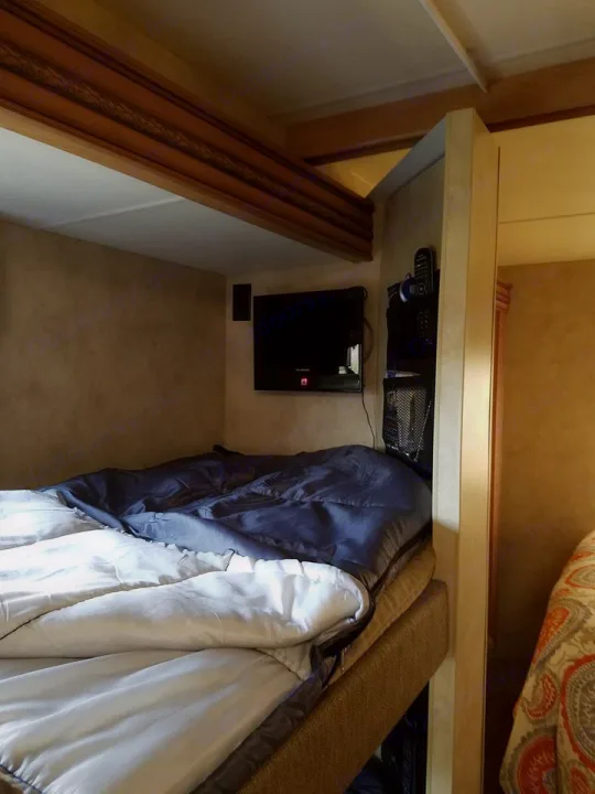 Inside an RV rental: a bunk bed with a sleeping bag, wall-mounted TV, and remote storage creates a cozy sleeping area.. Thor Motor Coach Chateau 2011