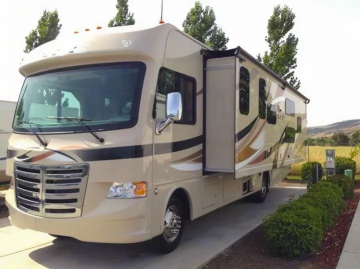 A spacious beige RV rental, with its slide-out extended, is parked at a sunny campsite, showcasing travel comfort.. THOR A.C.E 30.2 2015