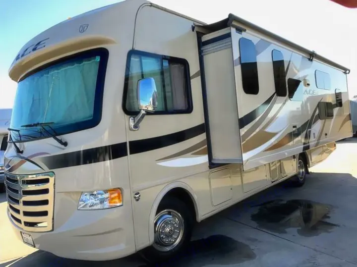 A cream-colored RV motorhome, available for rv rental, is parked with its side slide-out extended.. THOR A.C.E 30.2 2015