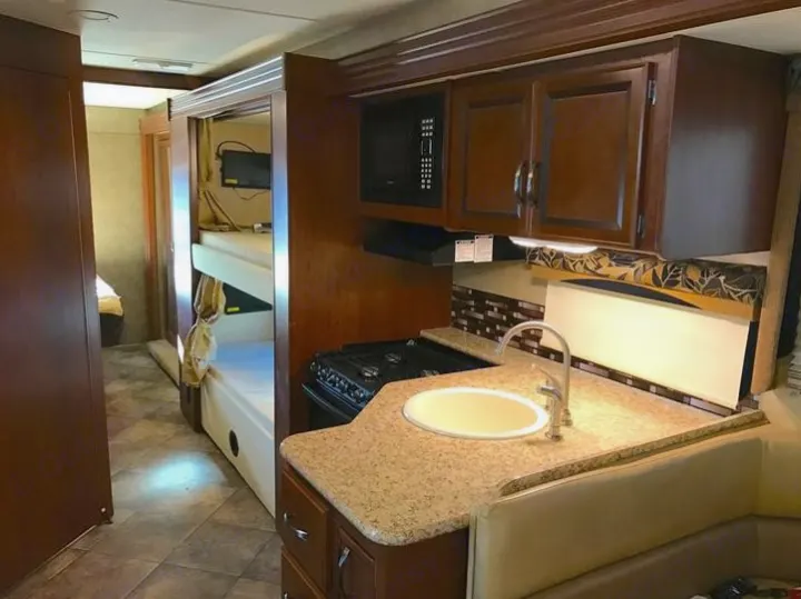 Well-appointed RV rental interior showcases a full kitchen (sink, stove, microwave), bunk beds, and a clear aisle.. THOR A.C.E 30.2 2015