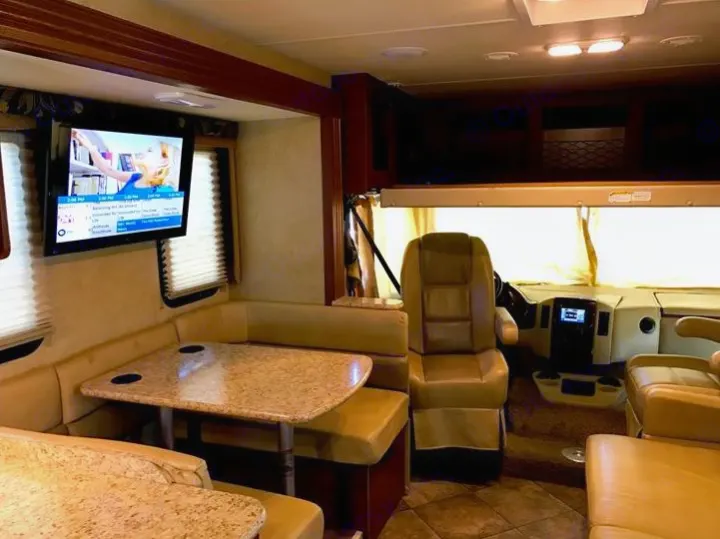 Spacious RV rental interior featuring a dinette with U-shaped seating, wall-mounted TV, and front cockpit with captain's chairs.. THOR A.C.E 30.2 2015