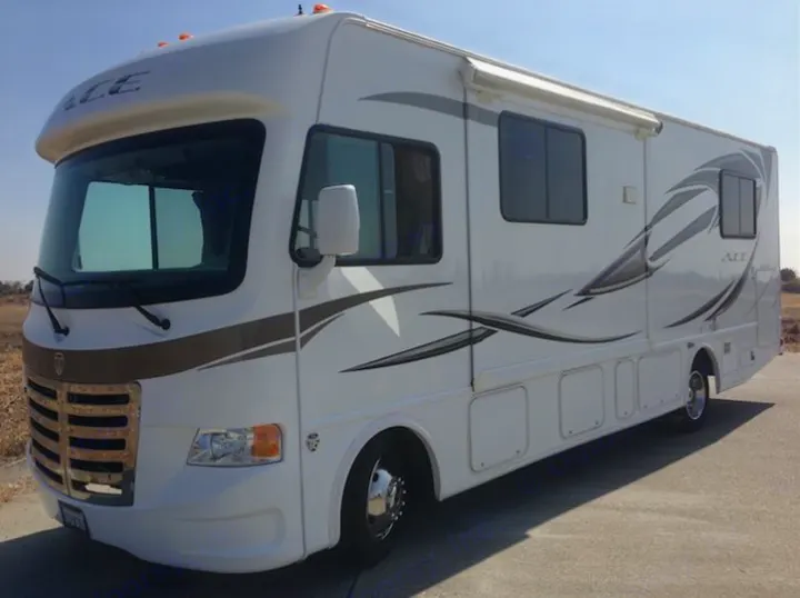 Full side view of a pristine white Thor ACE RV with graphic decals and an awning, perfect for rv rental.. THOR A.C.E. 29.1 2012