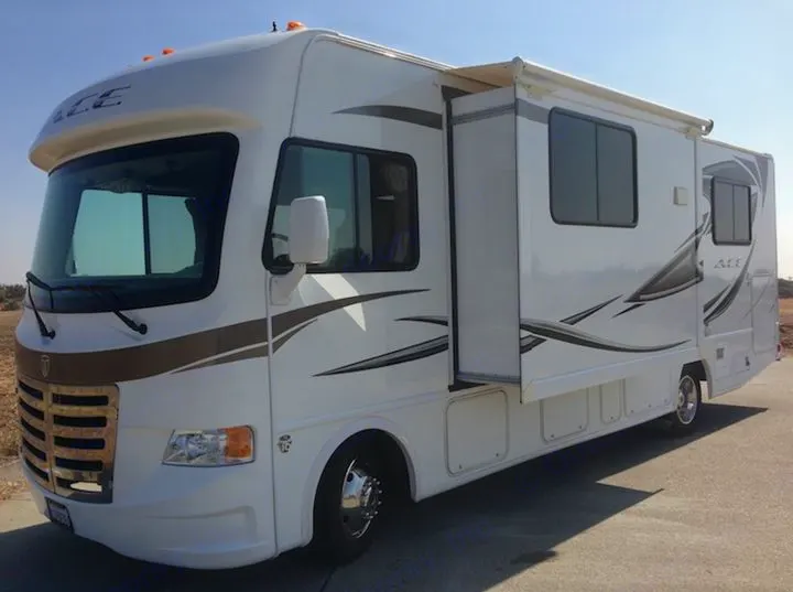 A large, white RV rental with brown and gray graphics, parked on asphalt. Its side slide-out is extended, ready for travel.. THOR A.C.E. 29.1 2012