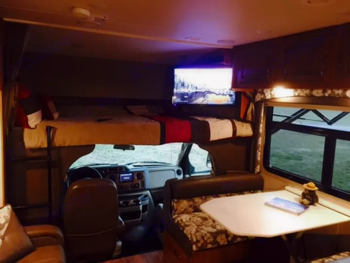 Comfortable RV rental interior featuring an overhead bed, dining table, driver's cockpit, and lounge area for your journey.. Jayco Greyhawk 2016