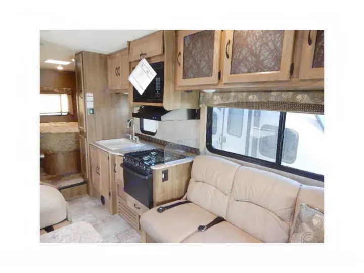RV rental interior view: compact kitchen with stove, sink, and microwave; plush sofa seating, and wooden cabinetry.. Coachmen Freelander 2017