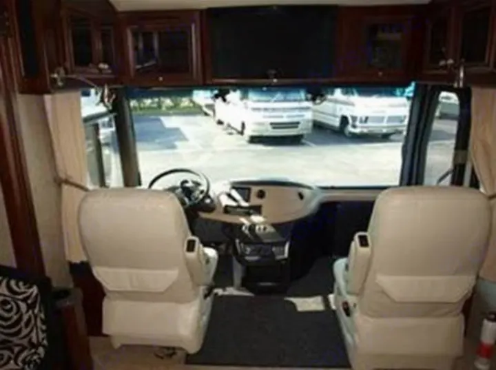 RV rental's inviting cockpit with plush driver/passenger seats, dashboard, and overhead TV. View outside shows other vehicles.. Fleetwood Revolution