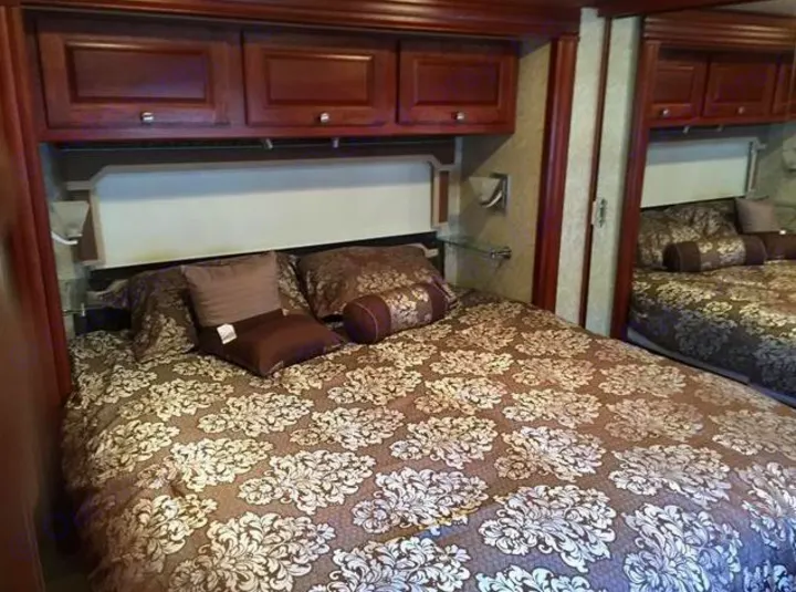 Cozy RV rental bedroom features a bed with a brown floral comforter, throw pillows, and dark wood overhead cabinets.. Winnebago Journey 2017