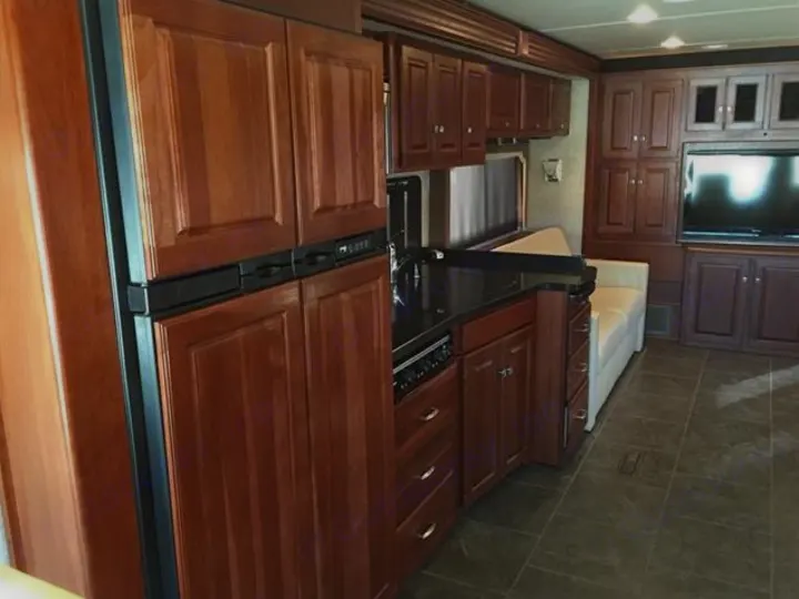 Spacious RV rental interior featuring polished wood cabinets, full kitchen, fridge, sofa, and TV in a comfortable living area.. Winnebago Journey 2017