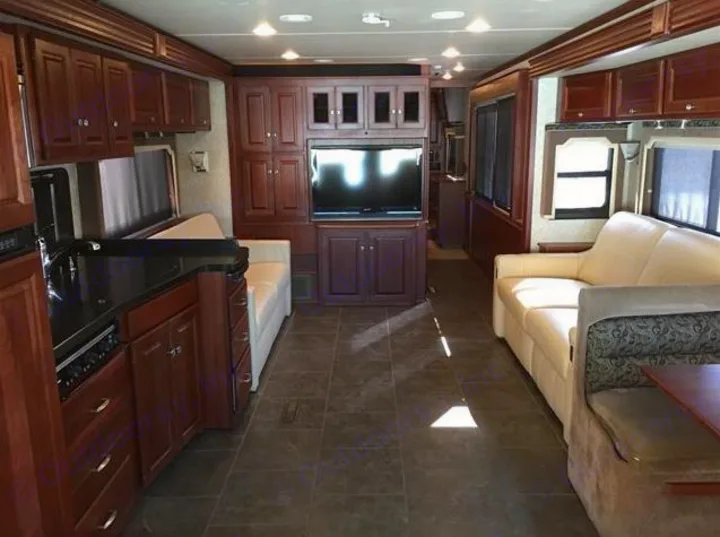 A full view of an RV rental's living area and kitchen, featuring light seating, dark wood cabinetry, and a central TV.. Winnebago Journey 2017