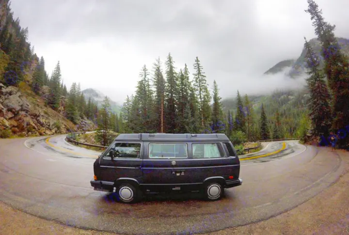 Dark RV rental parked on a winding mountain road among pine trees and foggy peaks.. Volkswagen Vanagon Camper 1988
