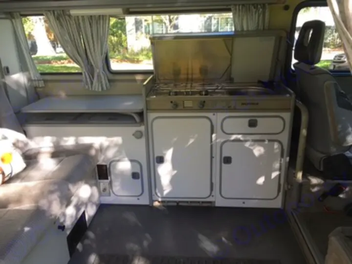 Inside a Westfalia RV rental: view of the compact kitchen with stove/sink & cabinets, next to the versatile sofa/bed area.. Volkswagen Vanagon Camper 1988