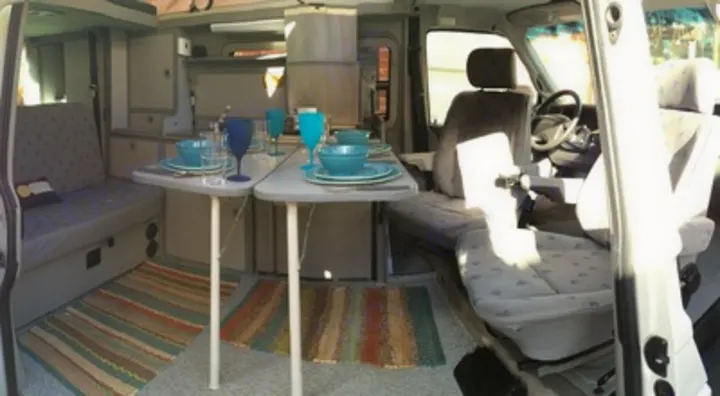 Spacious rv rental interior featuring a dining table set with blue dishes, kitchen, and seating area with rugs.. Volkswagen Eurovan Full Camper 2001