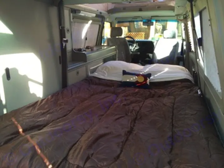 Comfortable RV rental camper van interior. Features a large bed & built-in cabinets, ideal for travel adventures.. Volkswagen Eurovan Full Camper 2001