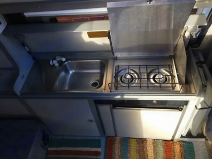 Compact RV rental kitchen: stainless sink, 2-burner stove, and small fridge. Practical for travel cooking.. Volkswagen Eurovan Full Camper 2001