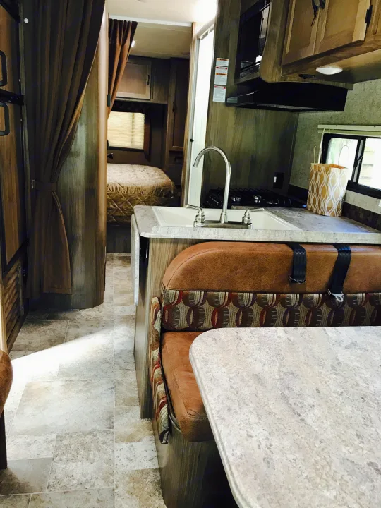 Inside an RV rental: view of the well-equipped kitchen, dinette with safety belts, and a cozy bedroom at the rear.. Coachmen Freelander 2017