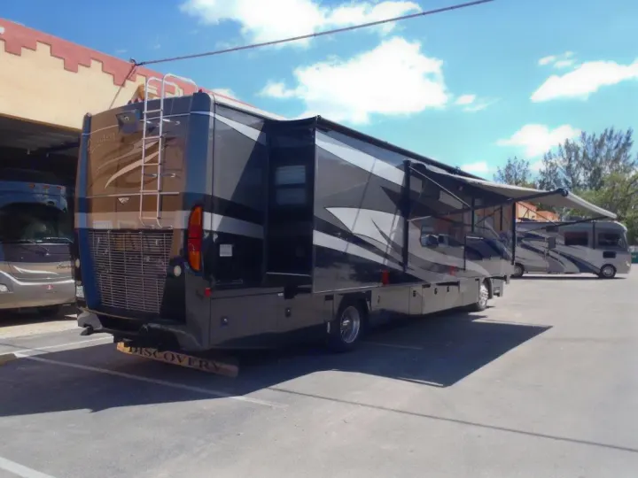 Large black RV rental with extended awnings & slide-out parked in a lot. Another motorhome is visible behind.. Fleetwood Discovery