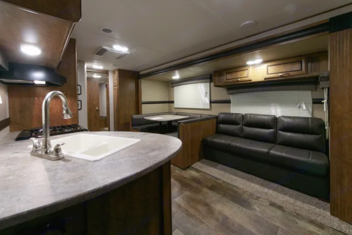 Spacious & modern RV rental interior with a functional kitchen, comfortable booth dining area, and a dark leather sofa.. Crossroads Zinger 2017